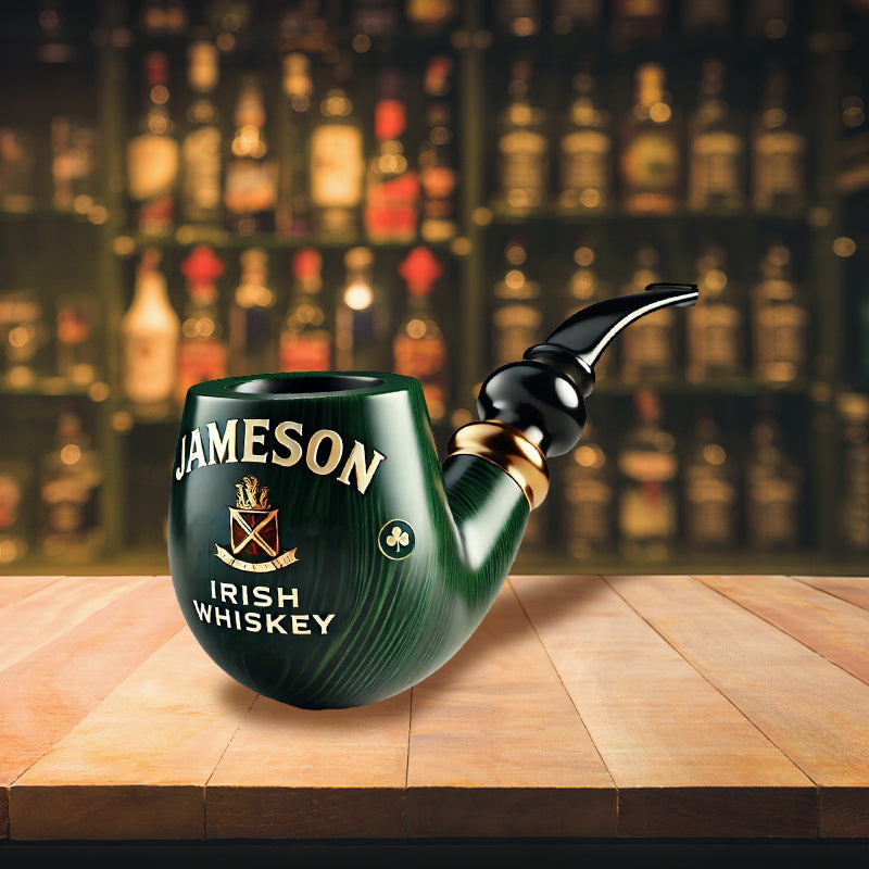Žalia, blizgi pypkė su „Jameson“ logotipu, medinė lentyna fone.