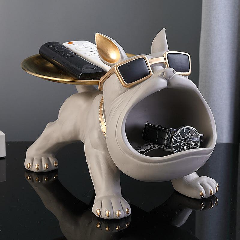 Bulldog-shaped holder, gray with gold accents, textured surface, holding remote and watch.