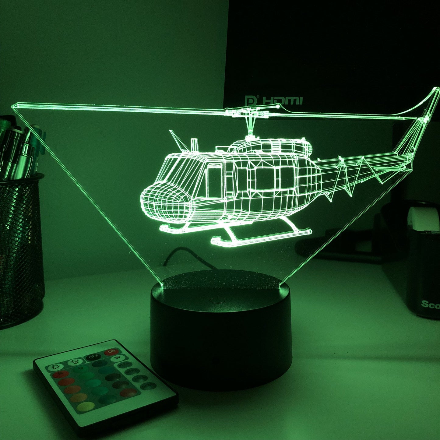 Žalias 3D sraigtasparnio modelis ant juodo pagrindo, šviečiantis tamsiame kambaryje.