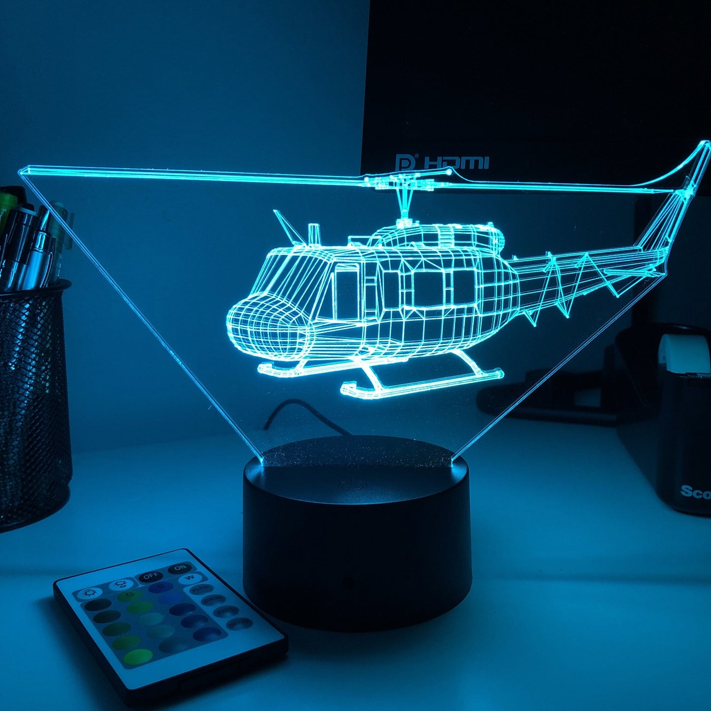 Mėlynas 3D sraigtasparnio holograminis šviestuvas ant juodo pagrindo, trikampio formos.