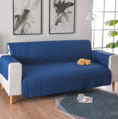 Mėlynas, siuvinėtas sofa užvalkalas su baltais porankiais ir medinėmis kojomis.