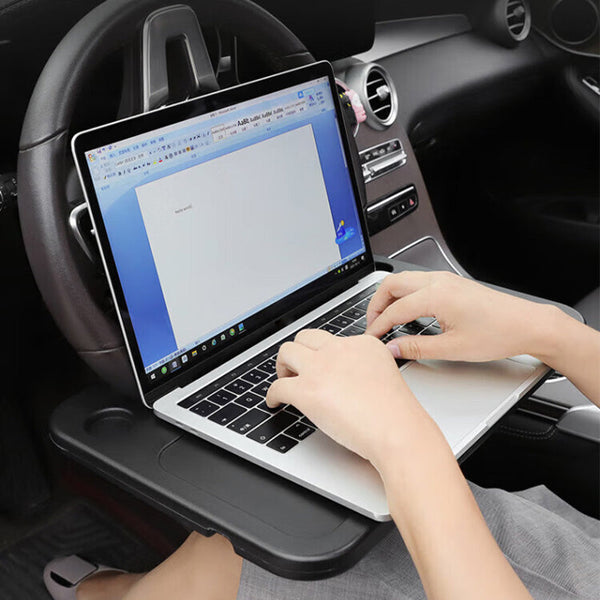Asmuo rašo nešiojamame kompiuteryje, padėtame ant juodo vairo stalo automobilyje.