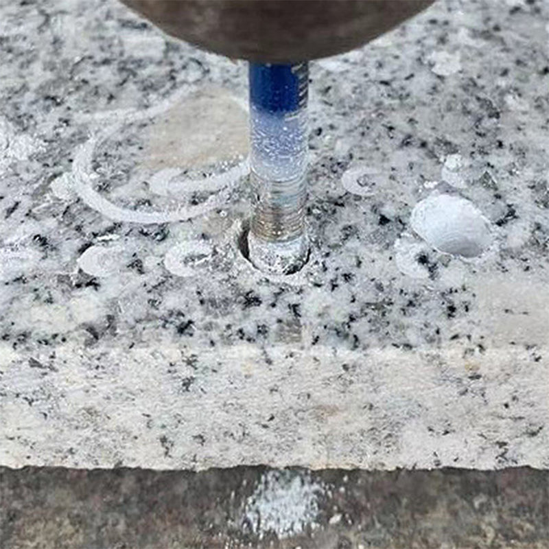 Gręžimo įrankis gręžia pilką granito paviršių, matomi balti dulkių pėdsakai.
