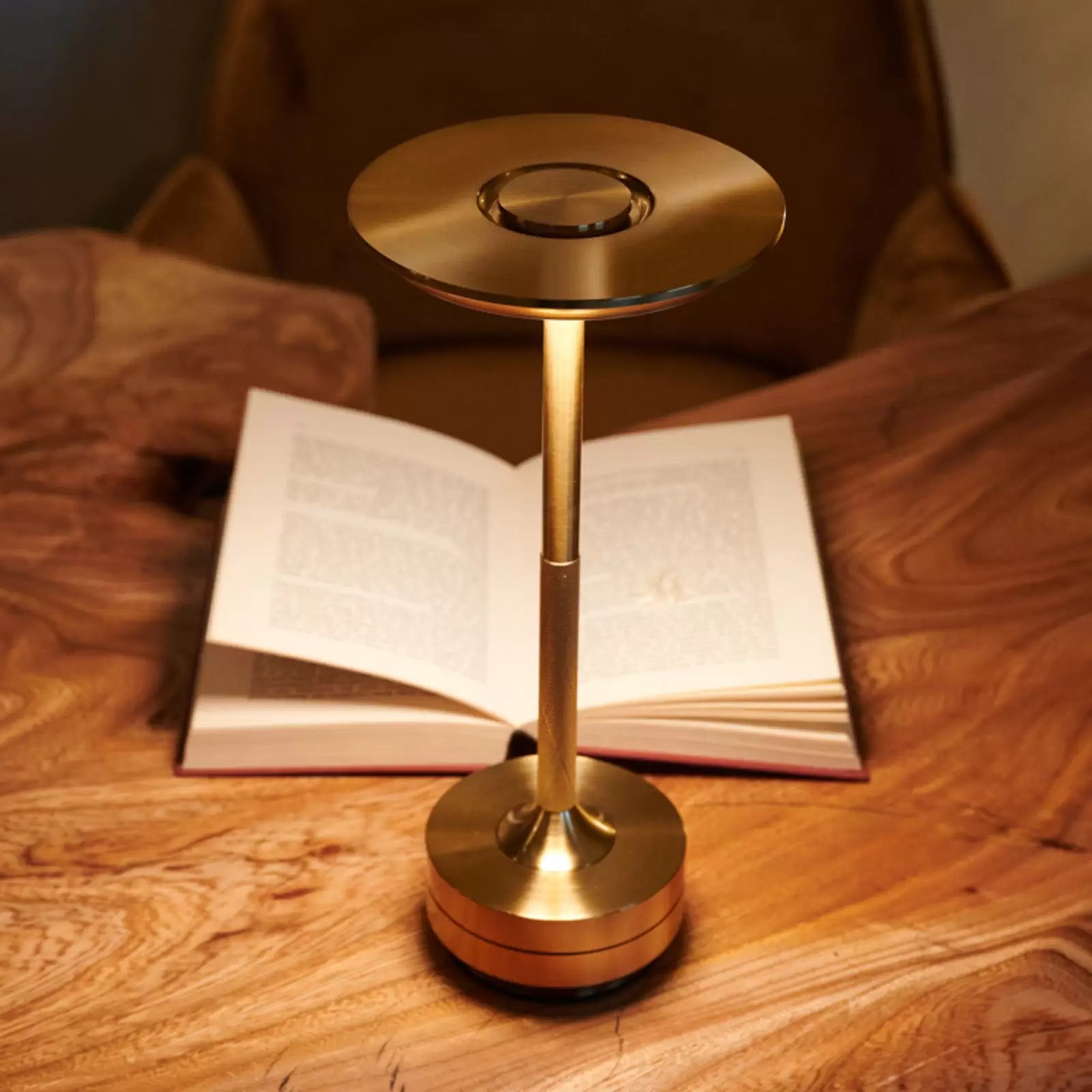 Aukšta auksinė lempa su apvaliu pagrindu, šviesi, blizgi, ant medinio stalo.