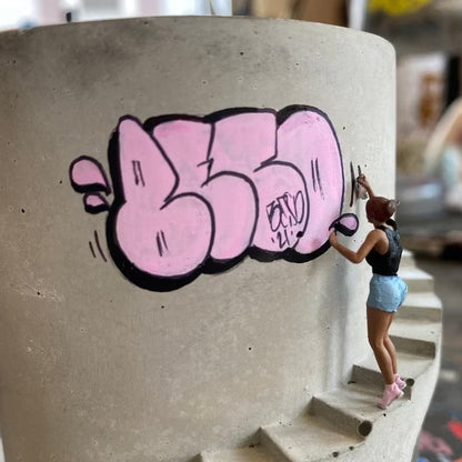 Graffiti vazonas su rožiniu užrašu ir figūrėle