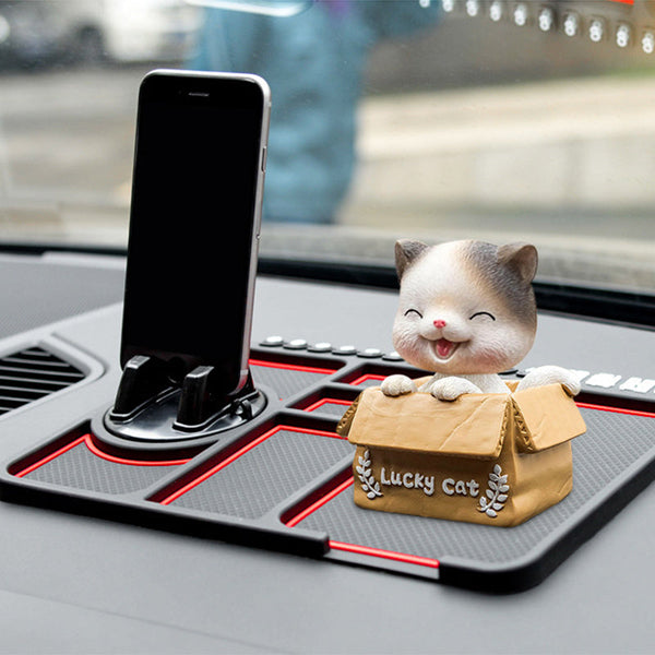 Juodas neslystantis kilimėlis ant automobilio panelės laiko telefoną, akinius ir dėžutę.