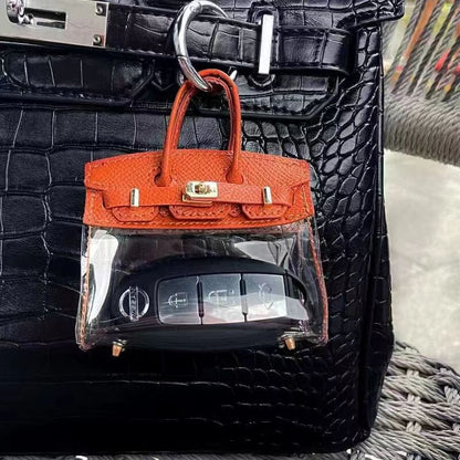 Oranžinis mini raktelių dėklas prisegtas prie juodos rankinės