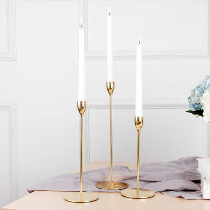 Aukšti auksiniai žvakidės su baltomis žvakėmis, švelni tekstūra, elegantiškas dizainas.