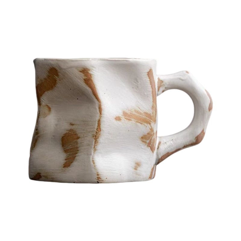 Nedidelis, kreivų formų baltas puodelis su rudais dėmėmis. Matinė tekstūra.