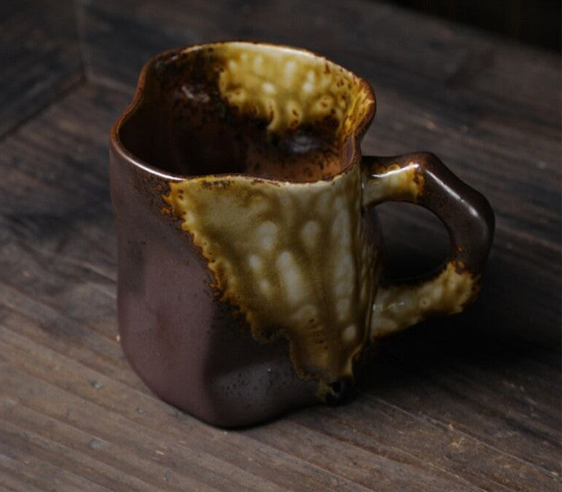 Nedidelis, nelygus keraminis puodelis, rudos ir geltonos spalvų, matinė tekstūra.