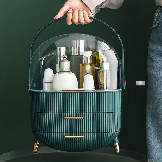 Žalias kosmetikos dėklas su skaidriu dangčiu ir dviem auksinėmis rankenėlėmis.