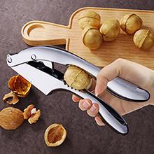 Nerūdijančio plieno riešutų skaldytuvas, laikomas rankoje, šalia graikinių riešutų.