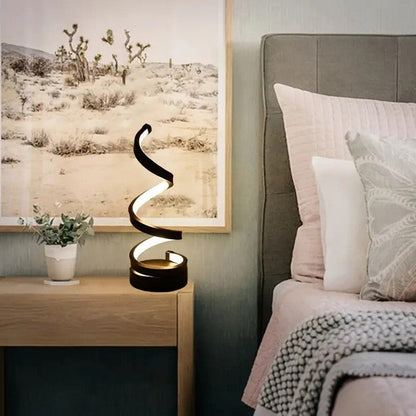 Juoda spiralė formos lempa su šviesos juosta, stovinti ant medinio stalo.