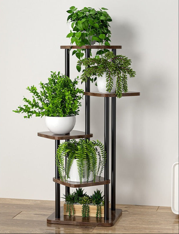 Aukštas, juodas metalinis stovas su medinėmis lentynomis ir žaliais augalais.