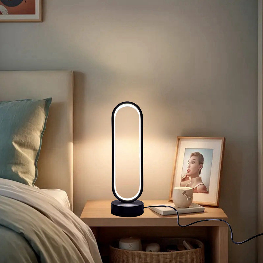 Moderni ovali stalinė lempa su juodu pagrindu ir šviesiu apšvietimu.