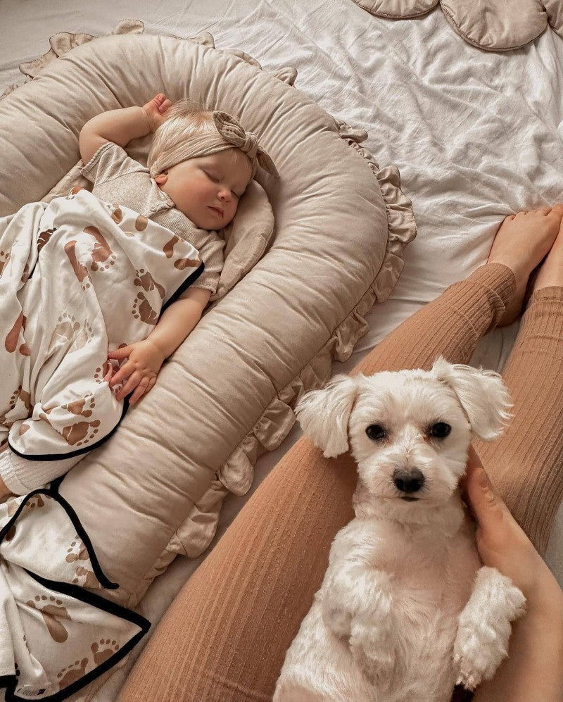 Miegantis vaikas minkštame, šviesiai rudos spalvos guolyje, šalia balto šuns.