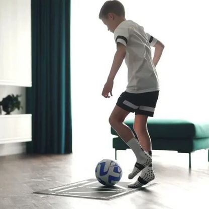 Berniukas treniruojasi su kamuoliu ant futbolo kilimėlio namuose