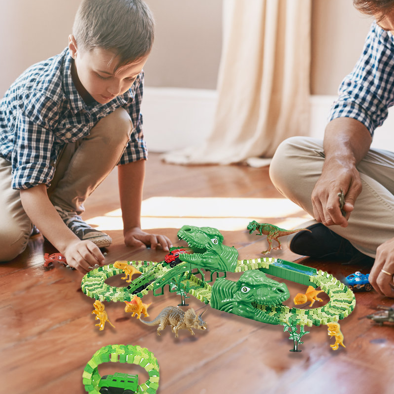 Du vaikai žaidžia su žaliais dinozaurų žaislais ant medinių grindų.