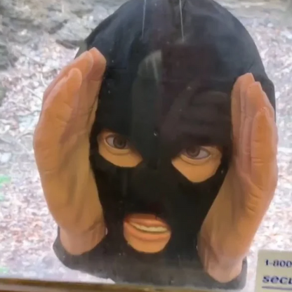Juoda veido kaukė su rankomis nufotografuota pro stiklą