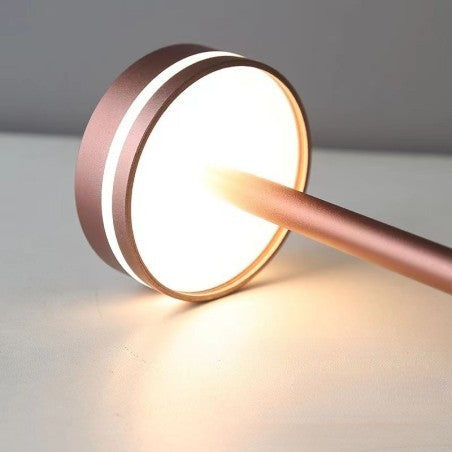 Rožinė stalinė lempa su apvaliu gaubtu ir šviesiu švytėjimu.