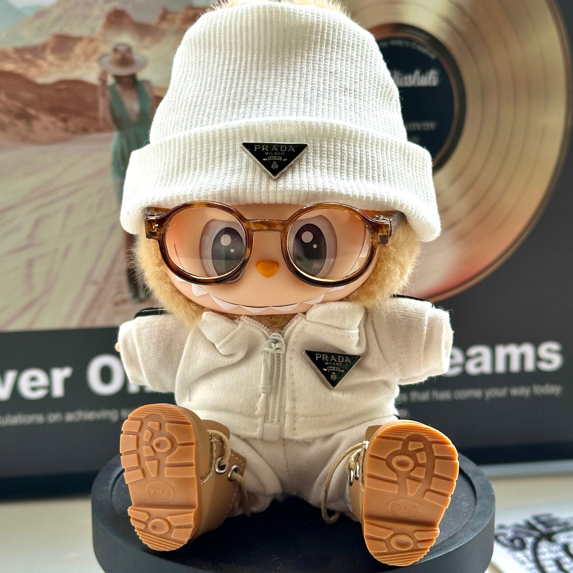 Labubu lėlė – apvalus rudas kailiukas, baltas trikotažinis megztukas, auksiniai akiniai, guminių batų padas