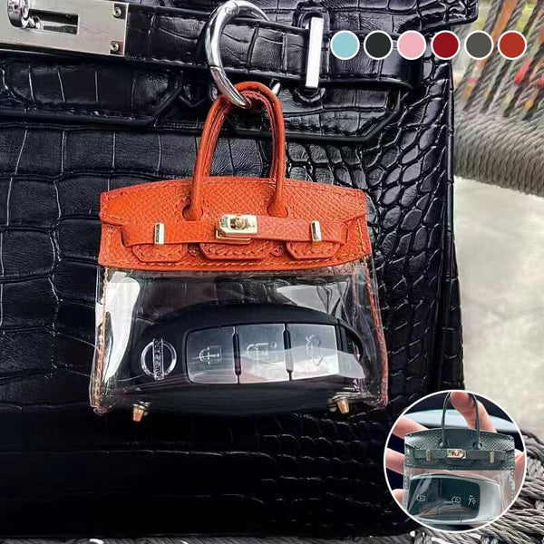 Oranžinis mini rankinės formos raktelių dėklas prisegtas prie rankinės