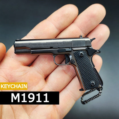 Juodas M1911 pistoleto formos raktų pakabukas delne.