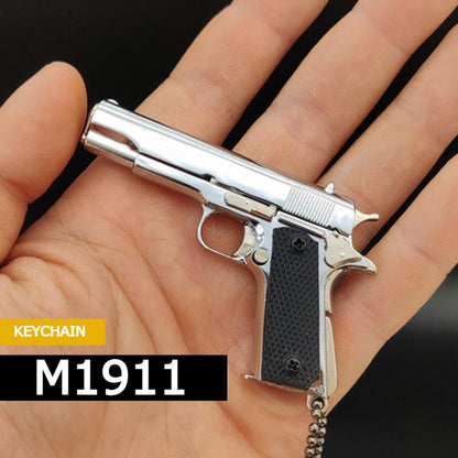 Sidabrinis M1911 pistoleto formos raktų pakabukas delne.