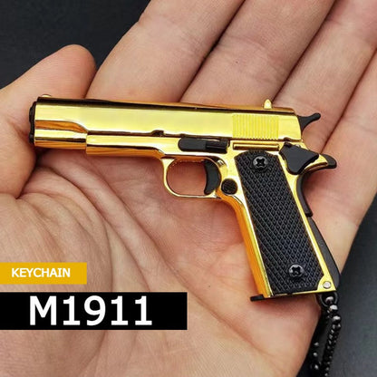 Aukso spalvos M1911 pistoleto formos raktų pakabukas delne.