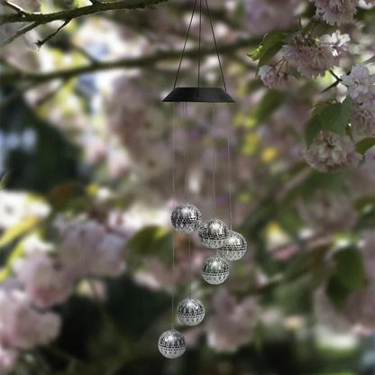 Saulės vėjo varpeliai su LED rutuliais – balti rutuliai prie žydinčio medžio